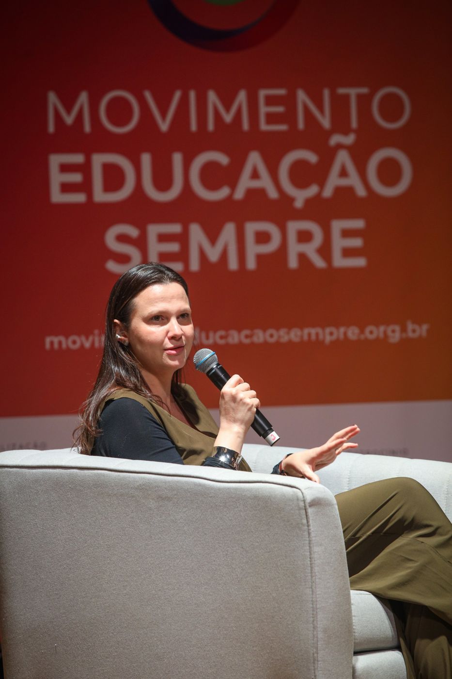 Juliana falando ao microfone em painel do Movimento Educação Sempre